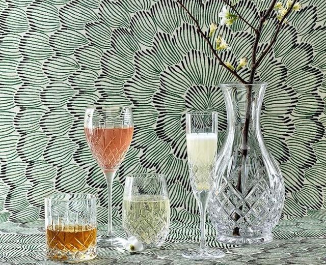 Las mejores copas de vino de cristal de Waterford en Bloomingdale’s, an assortment of crystal glasses and a crystal vase with a plant inside of it.